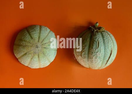 Cantaloupe sliced in half with whole cantaloupe isolated on orange background Stock Photo