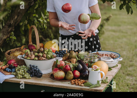 Woman standing by a table with fruit and vegetables throwing apples in the air, Serbia Stock Photo