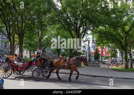 FOREIGN TOURISTS RIDING IN A HORSE AND CARRIAGE IN FRONT OF THE FOUNTAIN ON THE PLACE D'ARMES, QUEBEC, CANADA Stock Photo