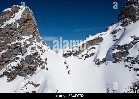 Three skiers hiking up a steep slope in the backcountry of the Gastein ski area, Salzburg, Austria Stock Photo