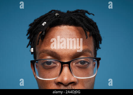 Close up portrait of contemporary African-American man wearing glasses and looking strongly at camera posing against blue background, copy space Stock Photo