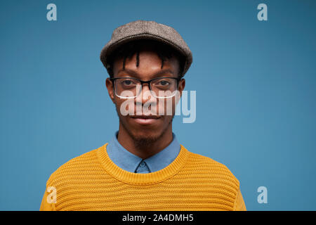 Head and shoulders portrait of contemporary African-American man looking at camera while wearing bright knit sweater and posing against blue backgroun Stock Photo