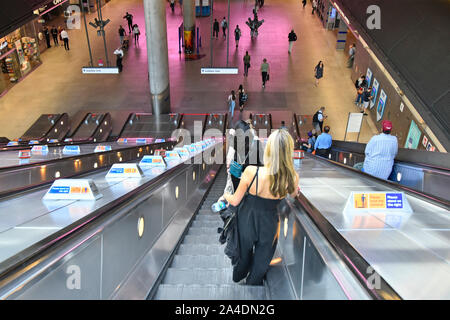 Back view young woman passenger descending on escalator to underground tube train services at Canary Wharf railway station London Docklands England UK Stock Photo