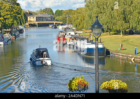 View of part of Great River Ouse at Ely with small motor boat passing moored narrowboat sunny summer afternoon Cambridgeshire East Anglia England UK