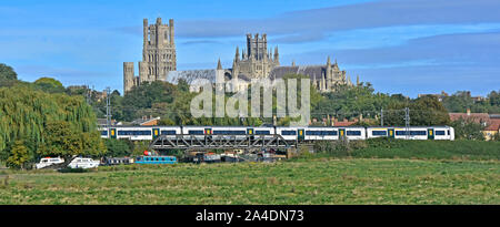 East Anglia panoramic Fens landscape boats moored on River Great Ouse below railway bridge train arrives Ely Station backdrop Ely Cathedral England UK Stock Photo