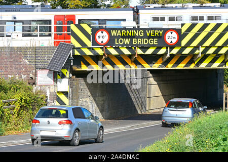 Close up of metric warning sign & black yellow hazard stripes painted on side of very low train railway bridge above cars driving into Ely England UK Stock Photo
