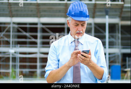 Senior engineer using his smartphone outdoor on a construction site Stock Photo