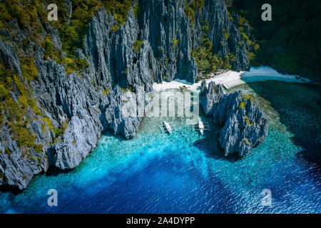 El Nido, Palawan, Philippines. Aerial above view of Secret hidden rocky lagoon beach with tourist banca boats in the cove surrounded by karst scenery