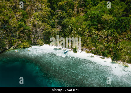 Aerial drone view of a secluded deserted tropical beach with lonely tourist boat surrounded by rainforest jungle. Cadlao Island, El Nido, Palawan Stock Photo