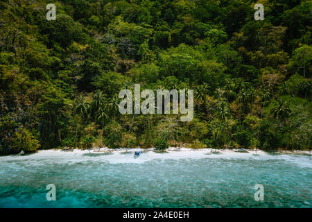 Palawan, Philippines, El Nido. Aerial drone view of a secluded deserted tropical beach with lonely tourist boat in frost of impressive rainforest Stock Photo