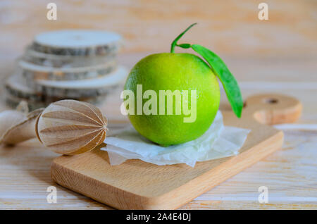 Organic green orange with green leaf onwood cut board, typical fruit grown on  Canary Islands and Vietnam. Citrus background. Stock Photo