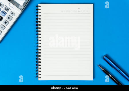 Open notebook with calculator and pen from top view on blue background. Stock Photo