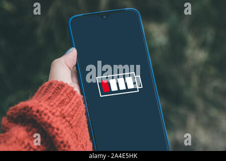 Top view of hand holding a smartphone with low battery on screen. Stock Photo