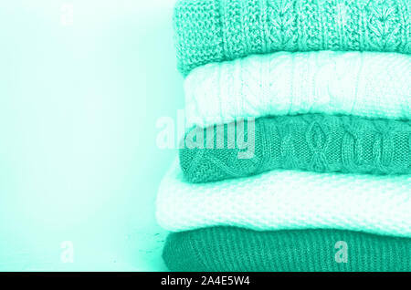 Pile of knitted wool sweaters in mint color background with copy space. Knitwear, clothes. Trendy green and turquoise color Stock Photo