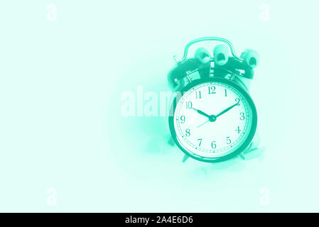Hand holding black alarm clock through hole in mint color background. Wake up alert concept. Trendy green and turquoise color. Morning routine. Banner Stock Photo