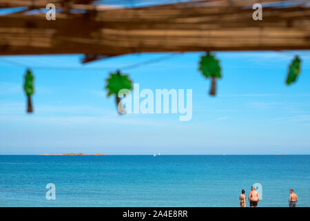 Palm tree shaped festive string lights on a rustic beach bar cafe with blue sea and sky beach with bathers - quirky tropical beach summer holiday Stock Photo