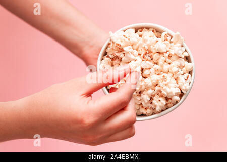 Woman eating popcorn. Popcorn in paper bag on pink background Stock Photo