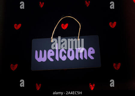 Welcome wording on black notice board  with red hearts around Stock Photo