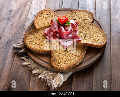 Cereal bread slices with bresaola flower on wooden table
