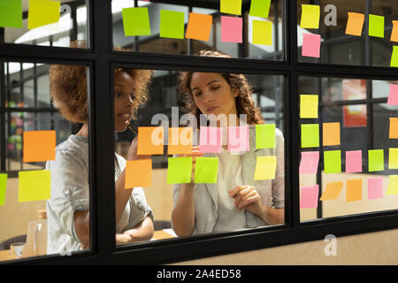 Diverse business women writing ideas on sticky notes working together Stock Photo