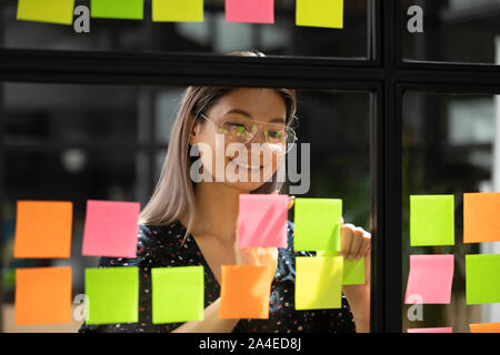 Asian businesswoman attached on glass sticky notes writes creative ideas Stock Photo