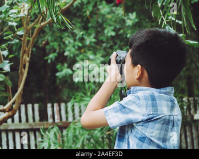 Young asian boy looking for attractive and taking photo by camera on forest background and nature holiday. Travel concept Stock Photo