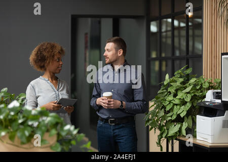 Multicultural businesspeople meet in office hallway walking and chatting Stock Photo