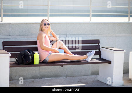 Sportswoman looking at smart phone, outdoors. Fitness female resting after run in the city. Stock Photo