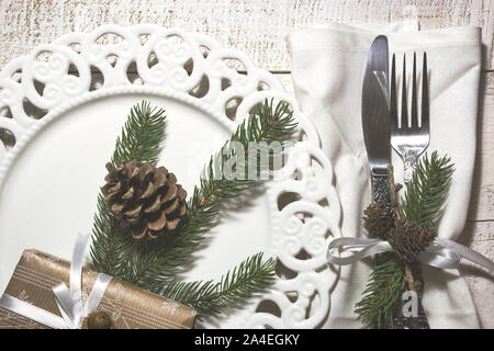 Festive table setting with vintage dishware, silverware, pine cone and branches decorations and gift box on rustic wooden table. Flat lay, top view, c Stock Photo