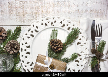 Festive table setting with vintage dishware, silverware, pine cone and branches decorations and gift box on rustic wooden table. Flat lay, top view, c Stock Photo