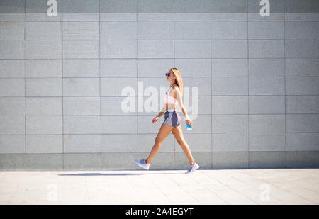 Young woman with fit body running against grey background. Female model in sportswear exercising outdoors. Stock Photo