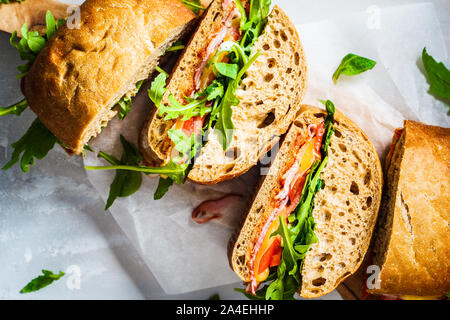 Ciabatta, cheese, ham and vegetable sandwiches on a wooden board. Stock Photo
