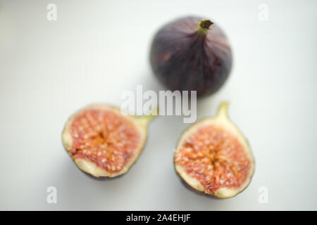 One whole fig and the second cut in half lie on a white table. Stock Photo