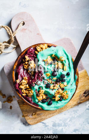 Healthy vegan breakfast. Spirulina and berries smoothie bowl with granola, gray background. Stock Photo