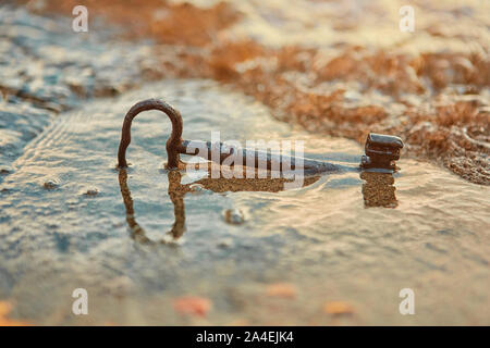 An old rusty lost treasure key, lying in the sand in the surf on the beach.  The concept of luck and unexpected wealth Stock Photo