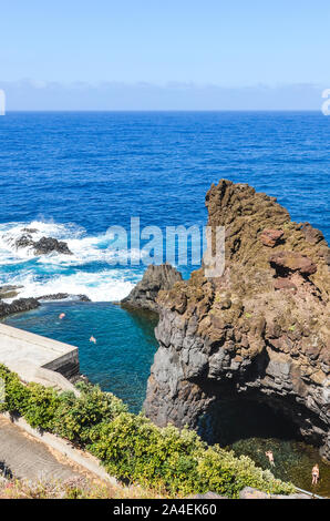 Tourists swimming in natural pools in the Atlantic ocean in Seixal, Madeira island, Portugal. Pool surrounded by volcanic rocks from the open sea. View from above. Summer vacation destination. Stock Photo