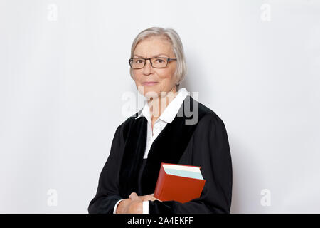 Female jurisdiction concept: mature german woman in a black judge's gown holding a legislative text book. Stock Photo