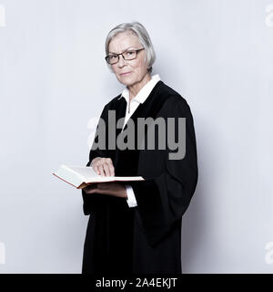 Female jurisdiction concept: mature german woman in a black judge's gown reading in a legislative text book. Stock Photo