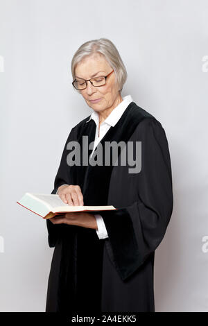 German jurisdiction concept: elderly judge in black robe reading in a book with the text of the german constitution. Stock Photo