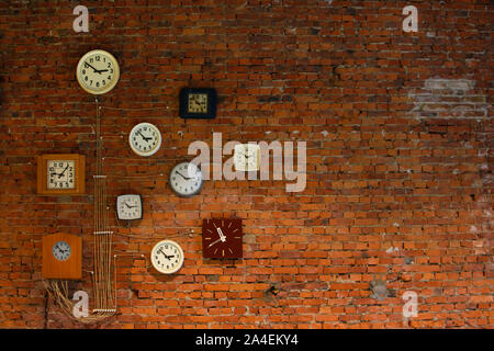 Collection of vintage wall clocks hanging on an old brick wall. Stock Photo