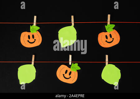 Background of halloween theme decorations. Toy pumpkins hanging on a string with wooden clothespins on black backdrop. Copy space. Flat lay style. Stock Photo