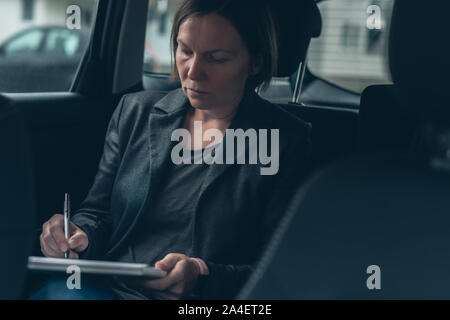 Businesswoman doing paperwork and analyzing business report while sitting in car at the back seat Stock Photo