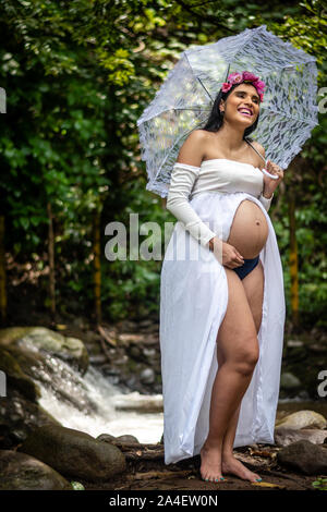 Beautiful latin pregnant woman 22-26 year old wearing white dress and holding umbrella Stock Photo