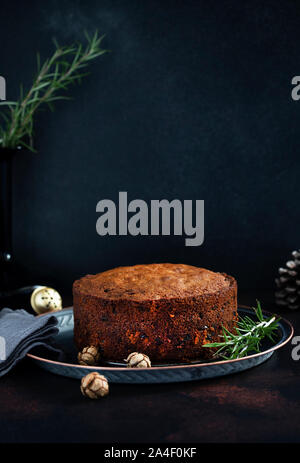 Traditional Christmas cake with fruits and nuts on a dark table and black background. Dessert for the winter holidays. Vertical. Copyspace Stock Photo