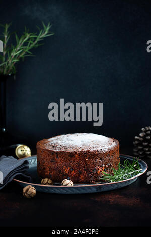 Traditional Christmas cake with fruits and nuts on a dark table and black background. Dessert for the winter holidays. Vertical. Copyspace Stock Photo