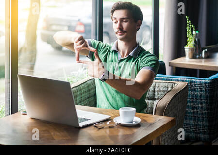 Focus on goals work. Young serious businessman in green t-shirt sitting and looking at laptop screen with crop composition gesture. business goals con Stock Photo
