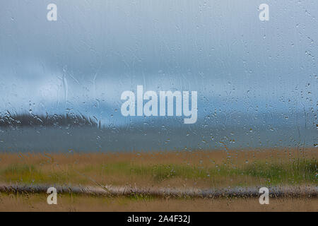 Rain drops on a large panoramic window looking out to sea on a stormy cloudy day Stock Photo