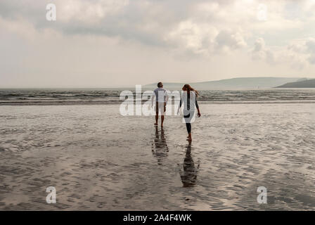 Couple walking on sandy beach leaving footprints in the sand. One father and his daughter enjoying the day. Cloudy day.