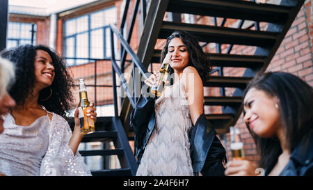 Young woman drinking beer from bottle surrounding by friends outdoors Stock Photo