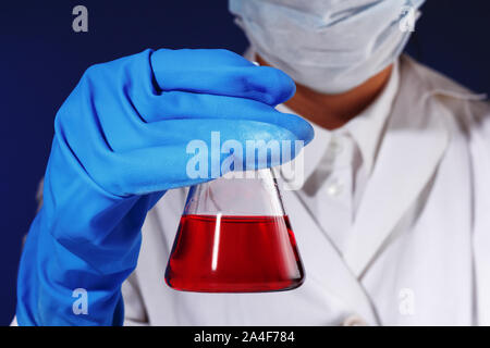 In a chemistry lab, a female chemist is analyzing a flask with red liquid. Medical experiment. Stock Photo